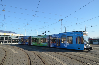 Das Bild zeigt die Demokratiestraßenbahn. Sie steht noch im Betriebshof Freiimfelder Straße. Die Bahn ist blau-grün beklebt. 